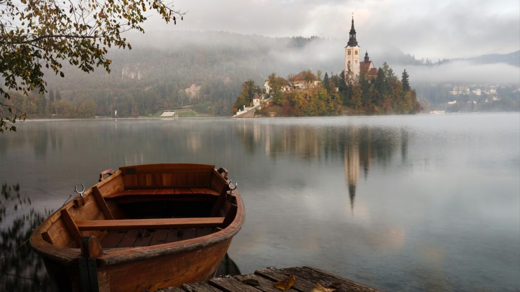 A small row boat on a lake. Across the lake is a small island with a building with tall towers on it.