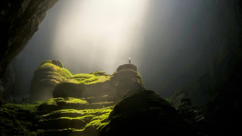 A figure stood on rocks in the distance illuminated by a beam of light.
